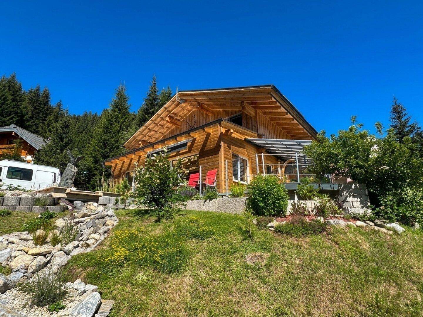 Attraktives Holzhaus mit gepflegtem Garten und Steinelementen, umgeben von grünen Bäumen.