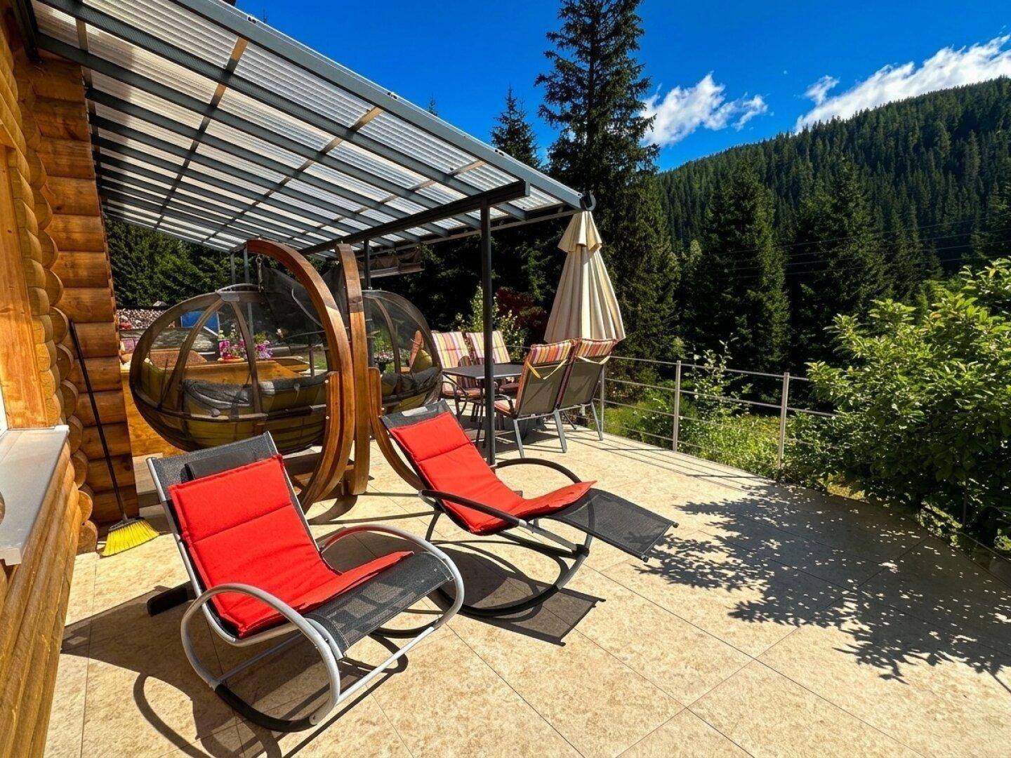 Überdachte Terrasse mit bequemen Liegestühlen und einer einzigartigen Sitzkugel, umgeben von Natur.