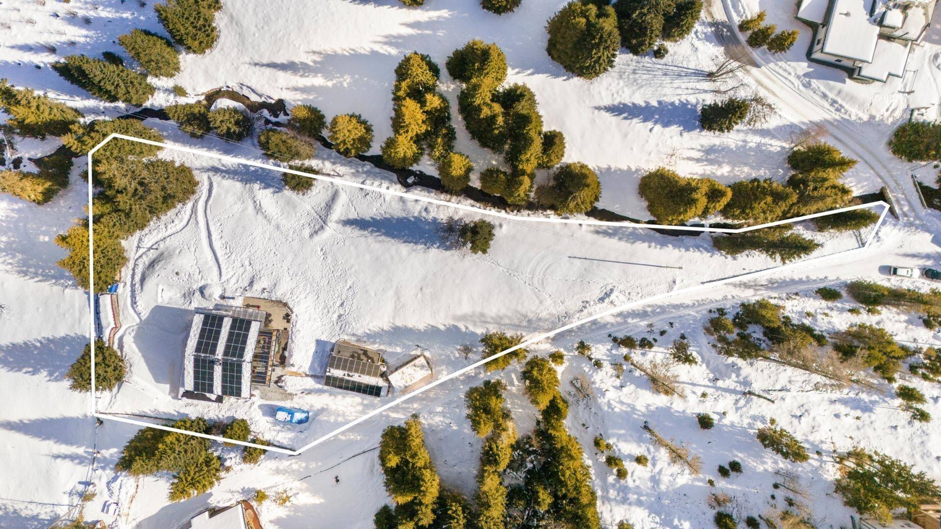 Luftaufnahme des Grundstücks in verschneiter Landschaft mit markierten Grenzen und umliegenden Wäldern.