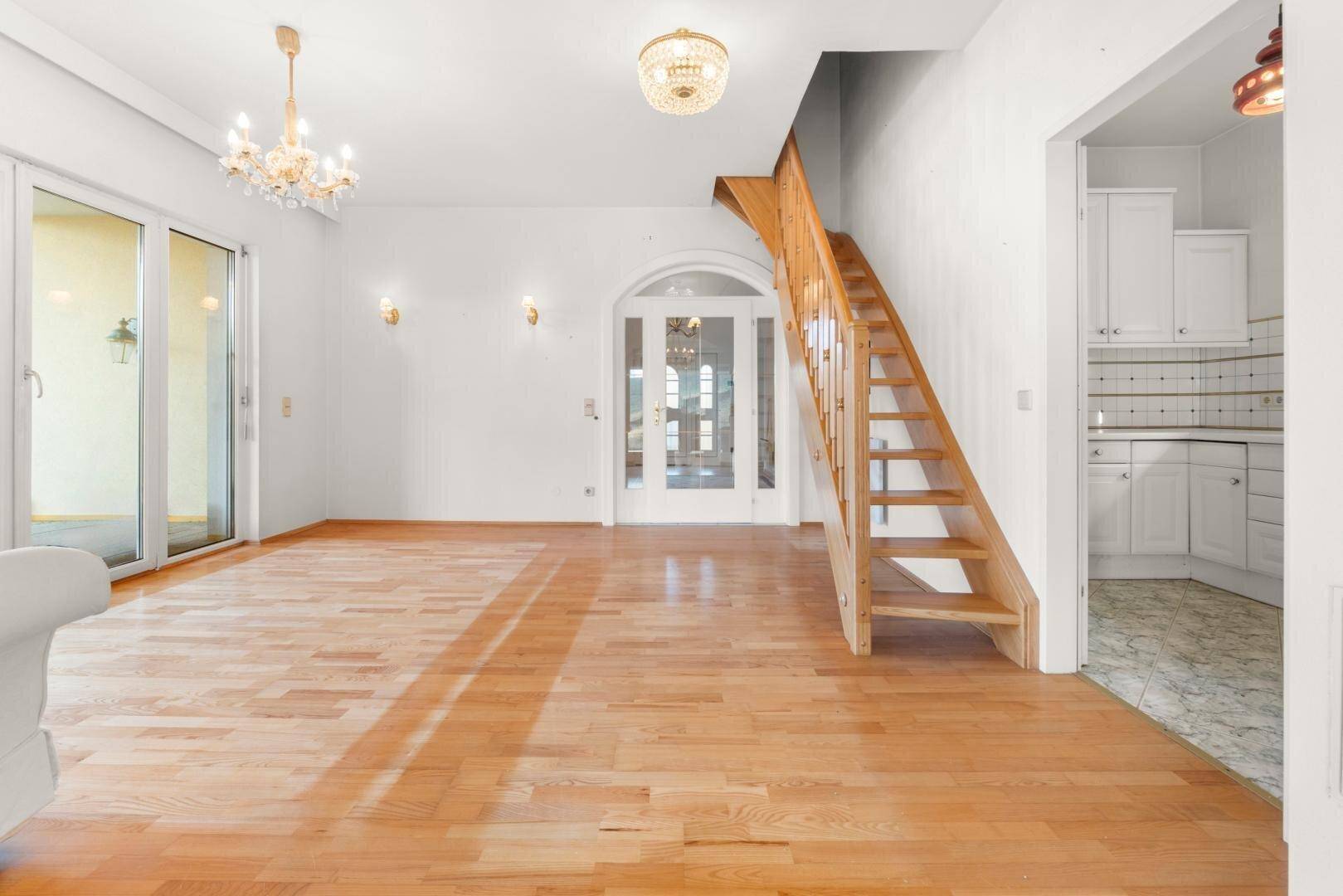 Geräumiges Wohnzimmer mit Holztreppe, Parkettboden und Zugang zu weiteren Räumen.
