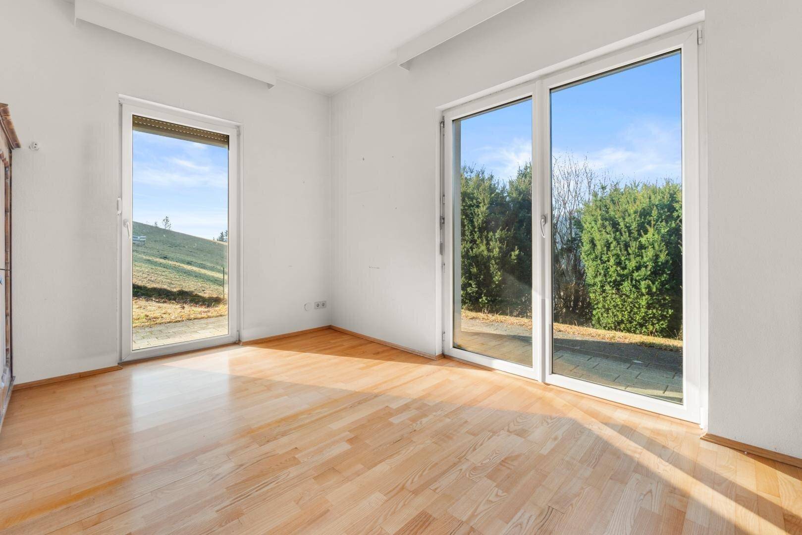 Heller Raum mit Holzboden und großen Fenstern, die viel Tageslicht hereinlassen.