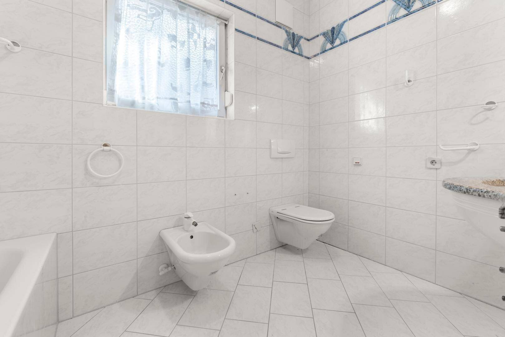 Badezimmer mit Bidet, WC, Fliesen und Fenster für natürliche Belüftung.