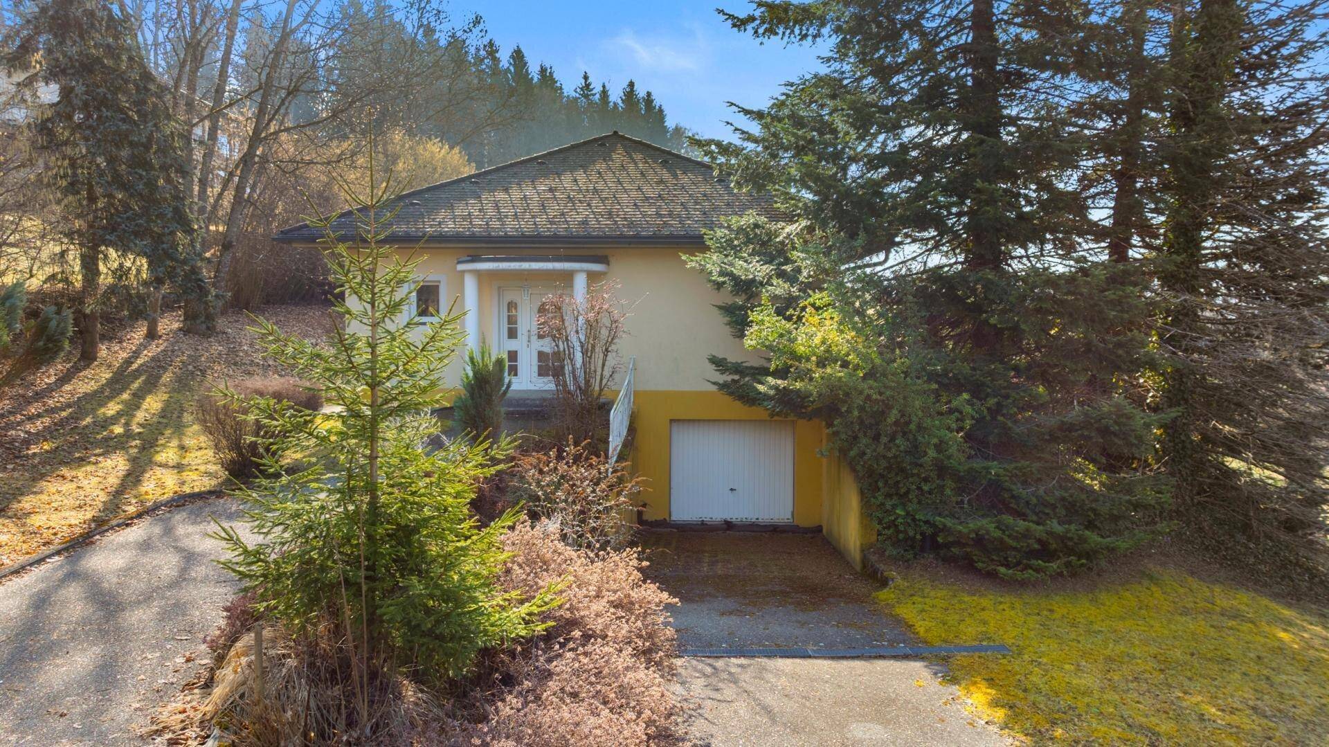 Einfamilienhaus mit Garage, Auffahrt und umgeben von Bäumen in ländlicher Umgebung.