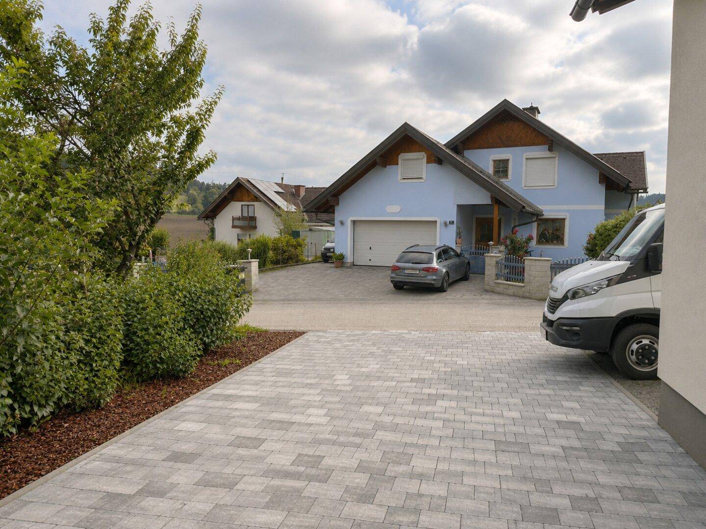 Gepflasterte Einfahrt mit einem geparkten Fahrzeug und Blick auf ein benachbartes Haus.