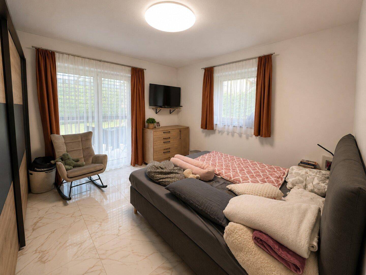 Helles Schlafzimmer mit Doppelbett, gemütlichem Sessel und direktem Zugang zu einem Außenbereich.