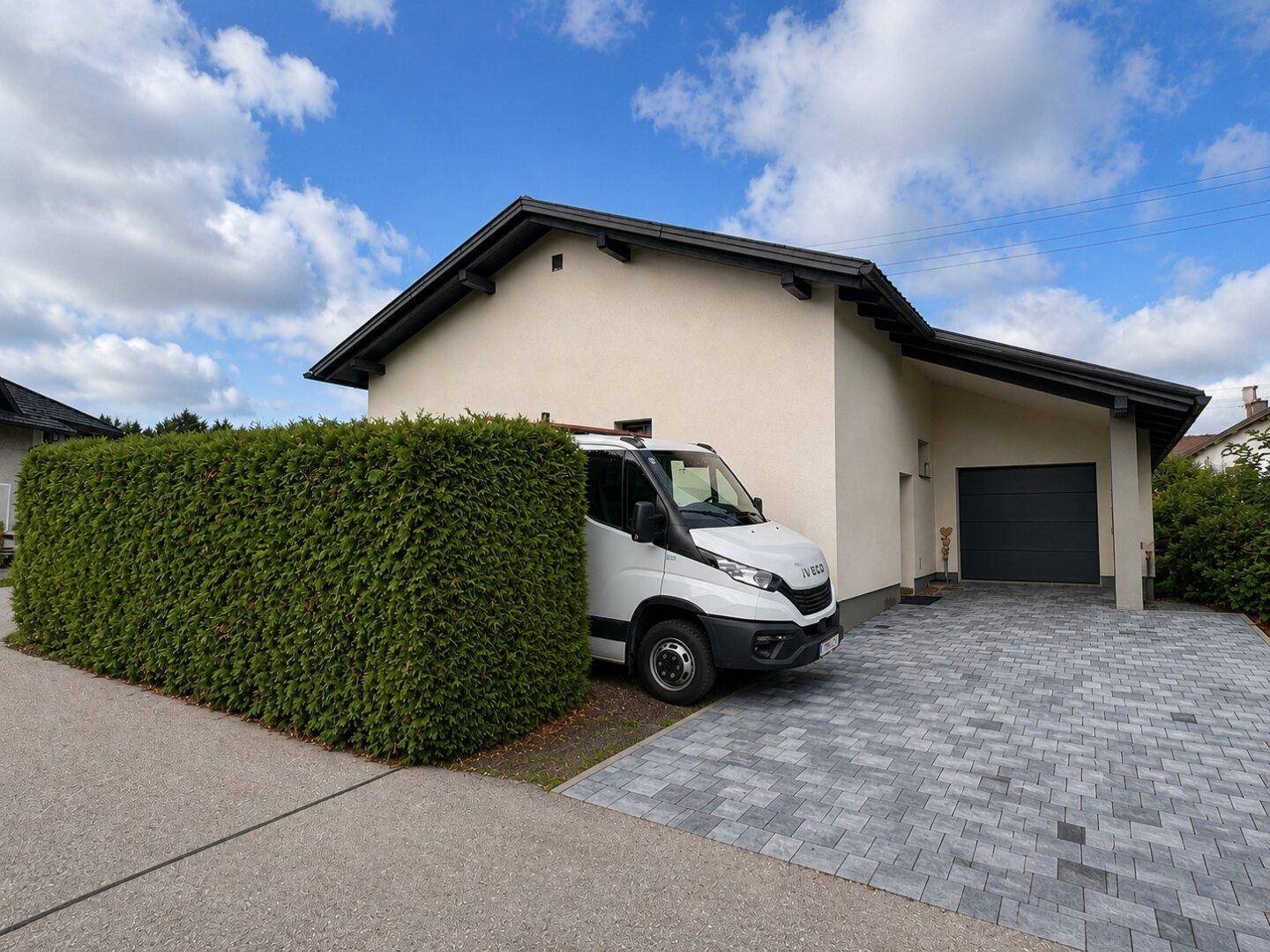 Gepflegte Einfahrt mit Hecke und einem geparkten Lieferwagen vor dem Haus.