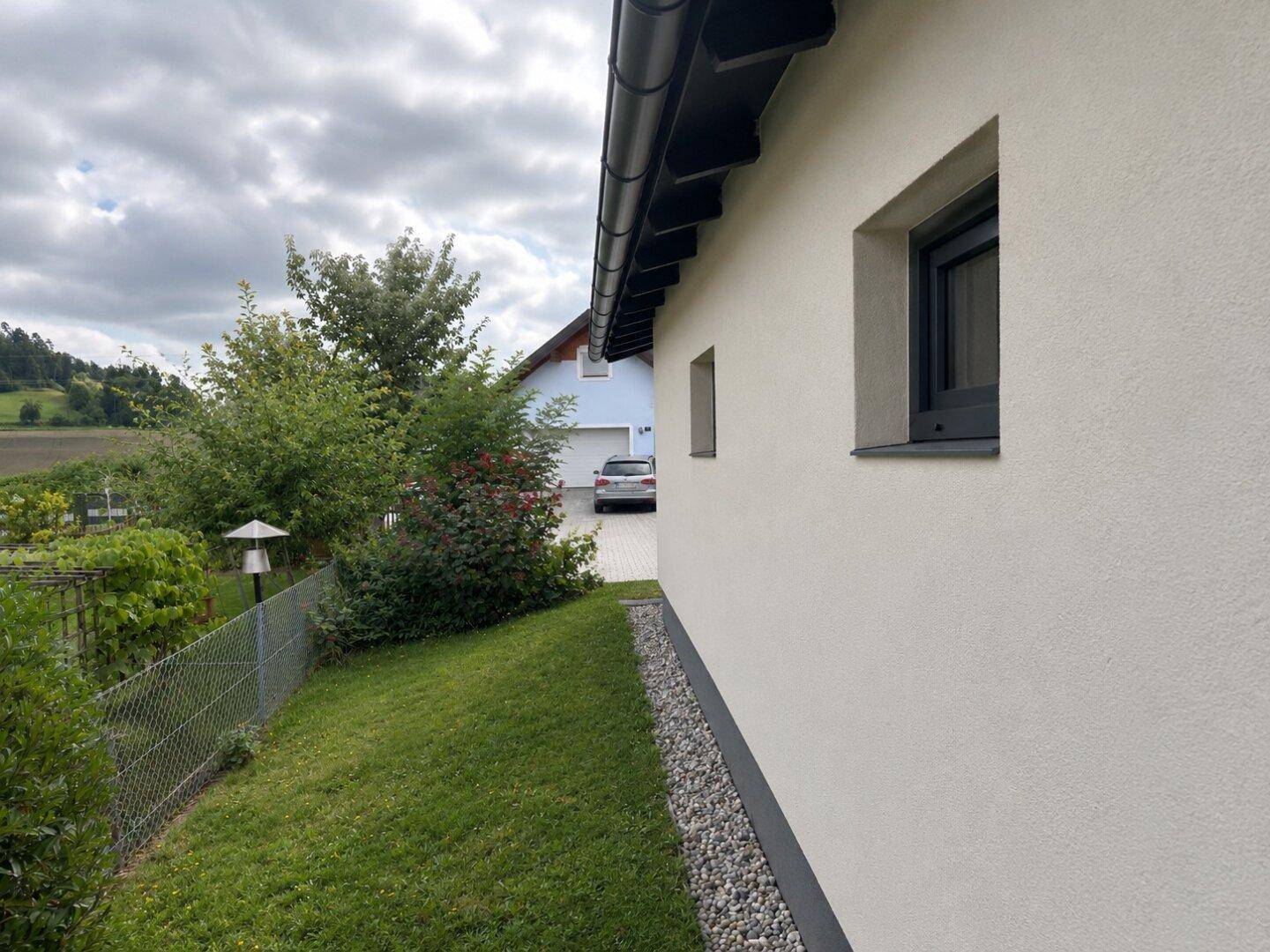 Seitenansicht des Hauses mit Blick auf die umliegende grüne Landschaft und einen Zaun.