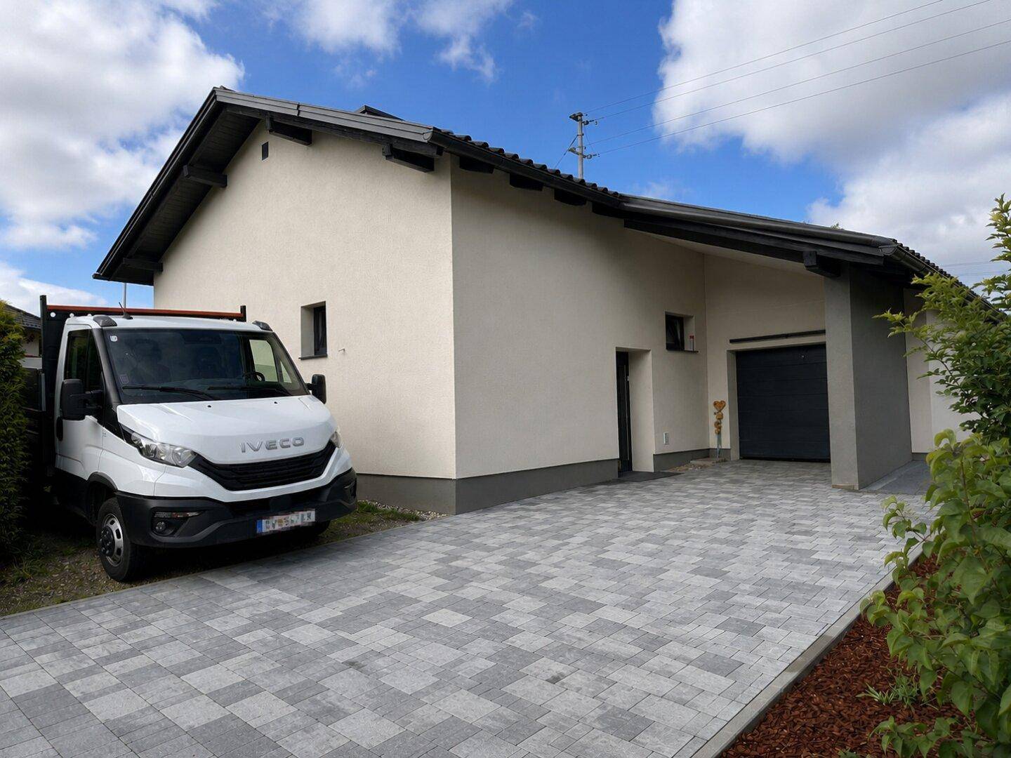 Vorderansicht des Hauses mit gepflasterter Einfahrt und einem geparkten Fahrzeug.
