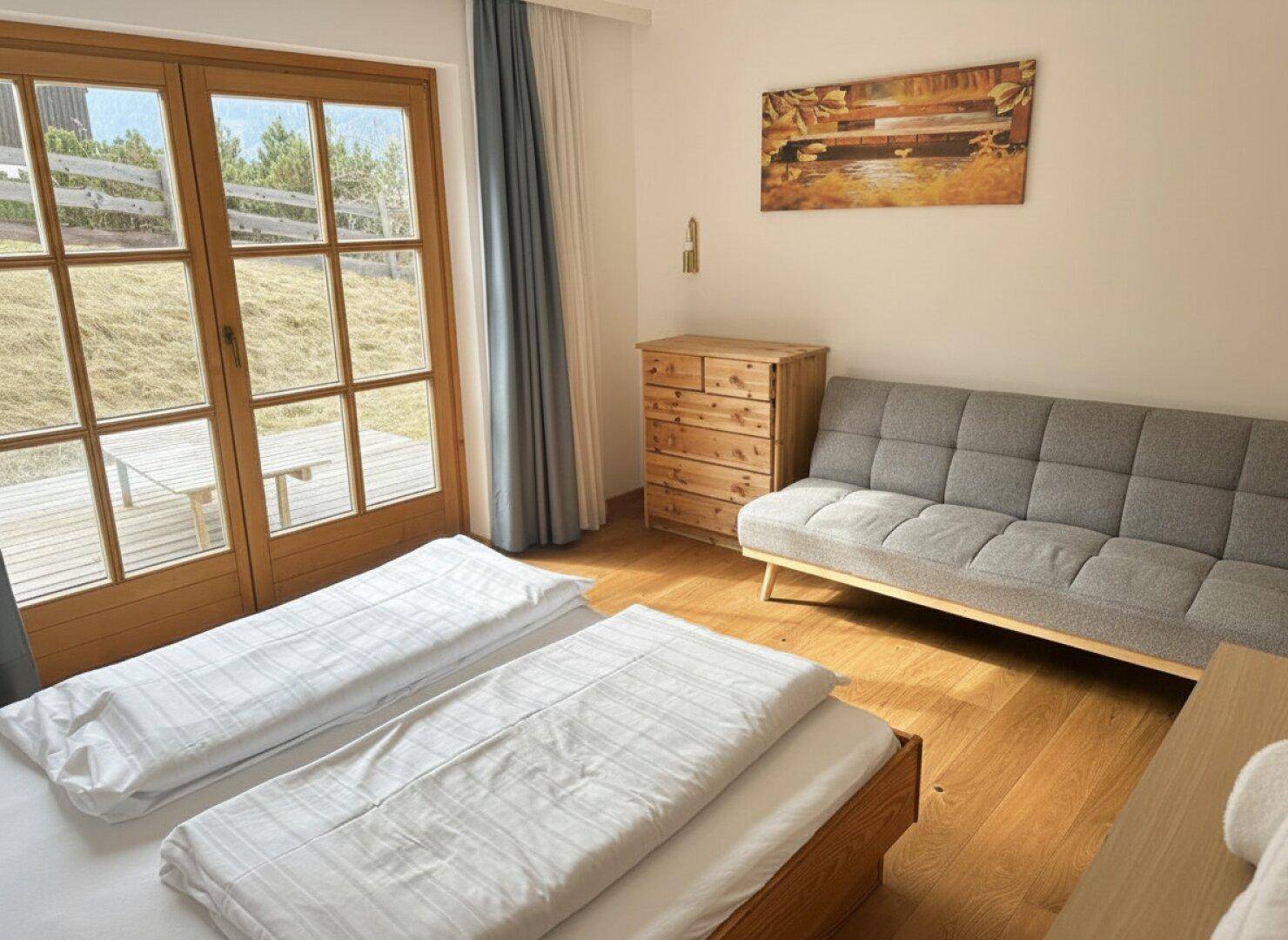 Gemütliches Schlafzimmer mit Sofa, Holzkommode und großen Fenstern mit Blick ins Grüne.