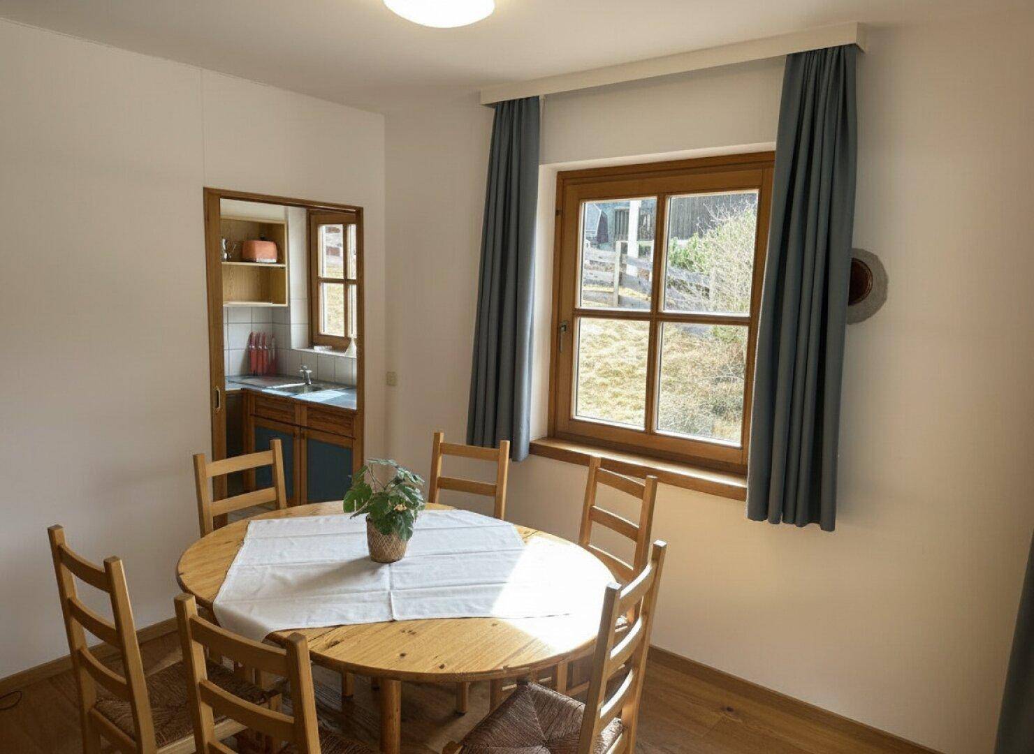 Rustikaler Essbereich mit Holztisch und Blick in die angrenzende Küche, hell durch Fenster.