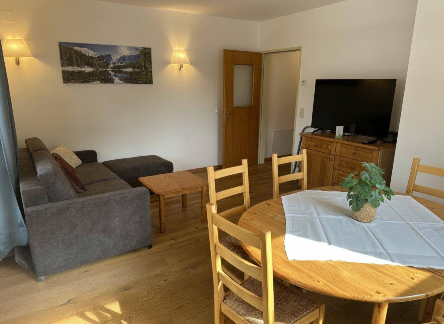 Wohnbereich mit bequemer Couch, Fernseher und Essgruppe, durchflutet von natürlichem Licht.