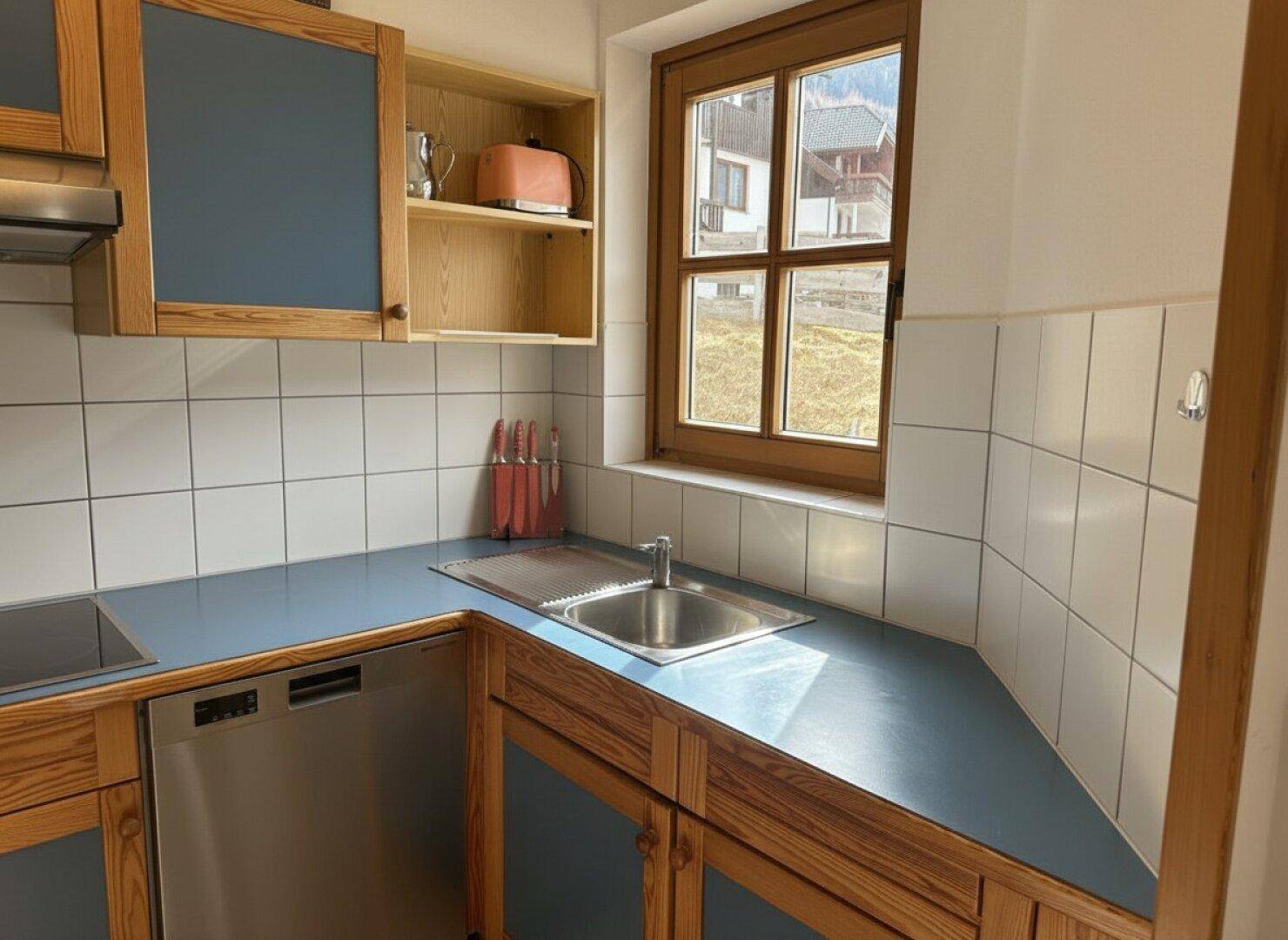 Funktionale Küche mit blauen Arbeitsplatten, Holzschränken, Spüle und Geschirrspüler, mit Fenster.