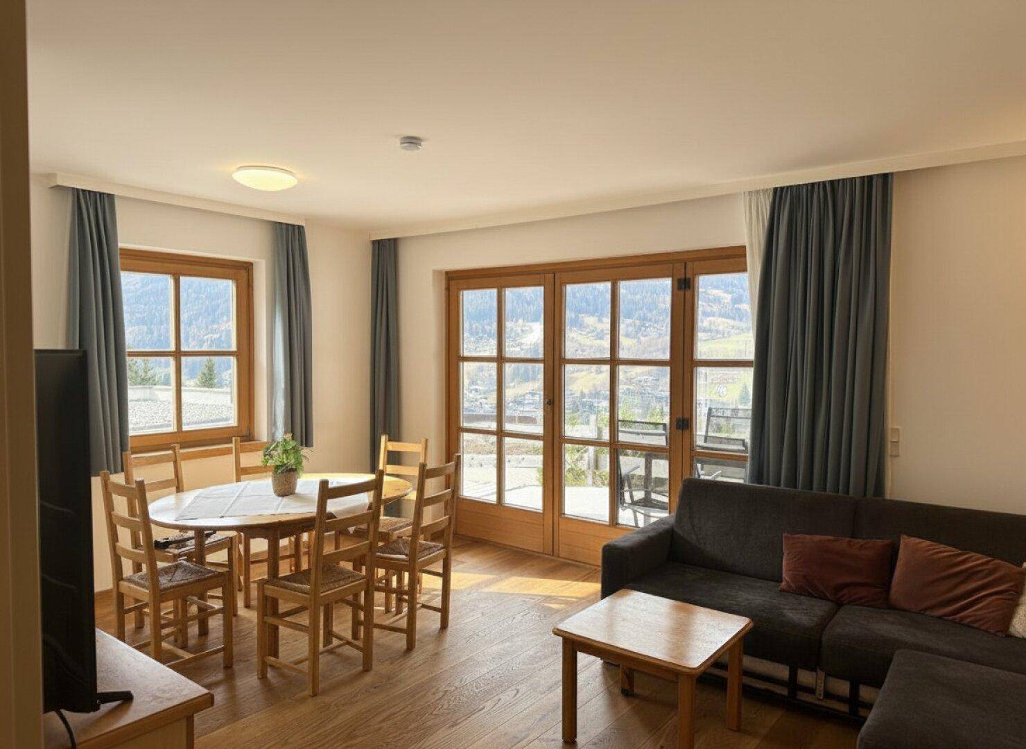 Offener Wohn-Essbereich mit Holzboden, Esstisch und Zugang zu einem Balkon mit Bergblick.