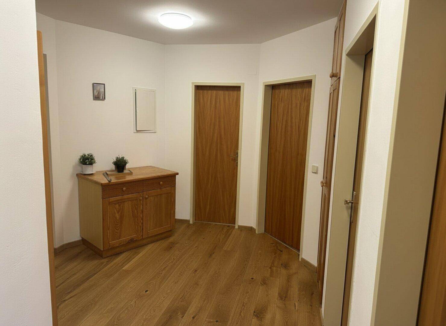 Heller Flur mit Holzboden und einer Holzkommode, der zu verschiedenen Räumen führt.