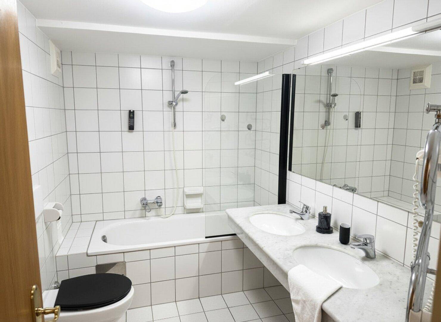 Modernes Badezimmer mit weißen Fliesen, Badewanne mit Dusche und Doppelwaschbecken.
