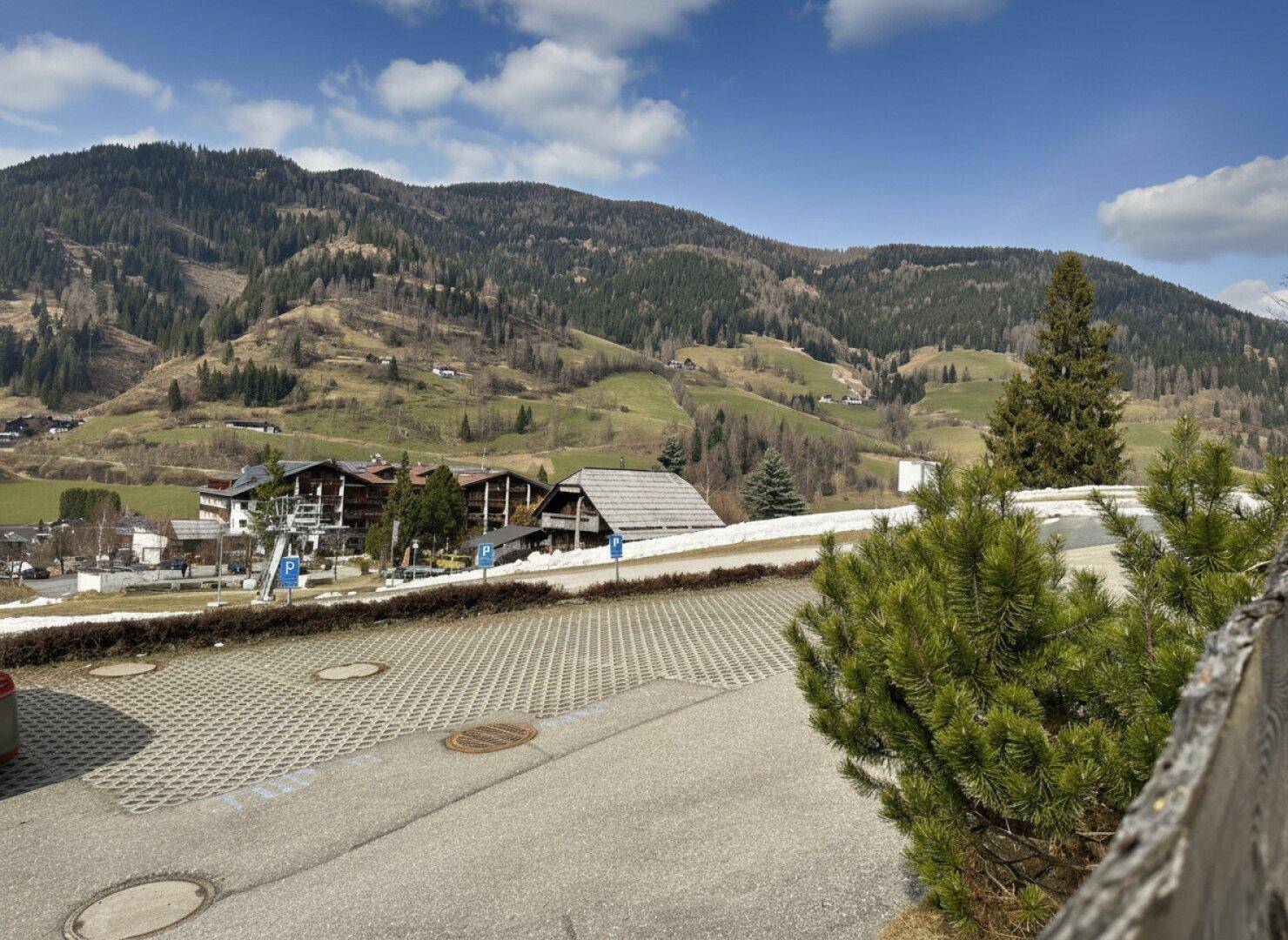 Großer Parkplatz mit Blick auf die umliegende Berglandschaft und grüne Hügel.