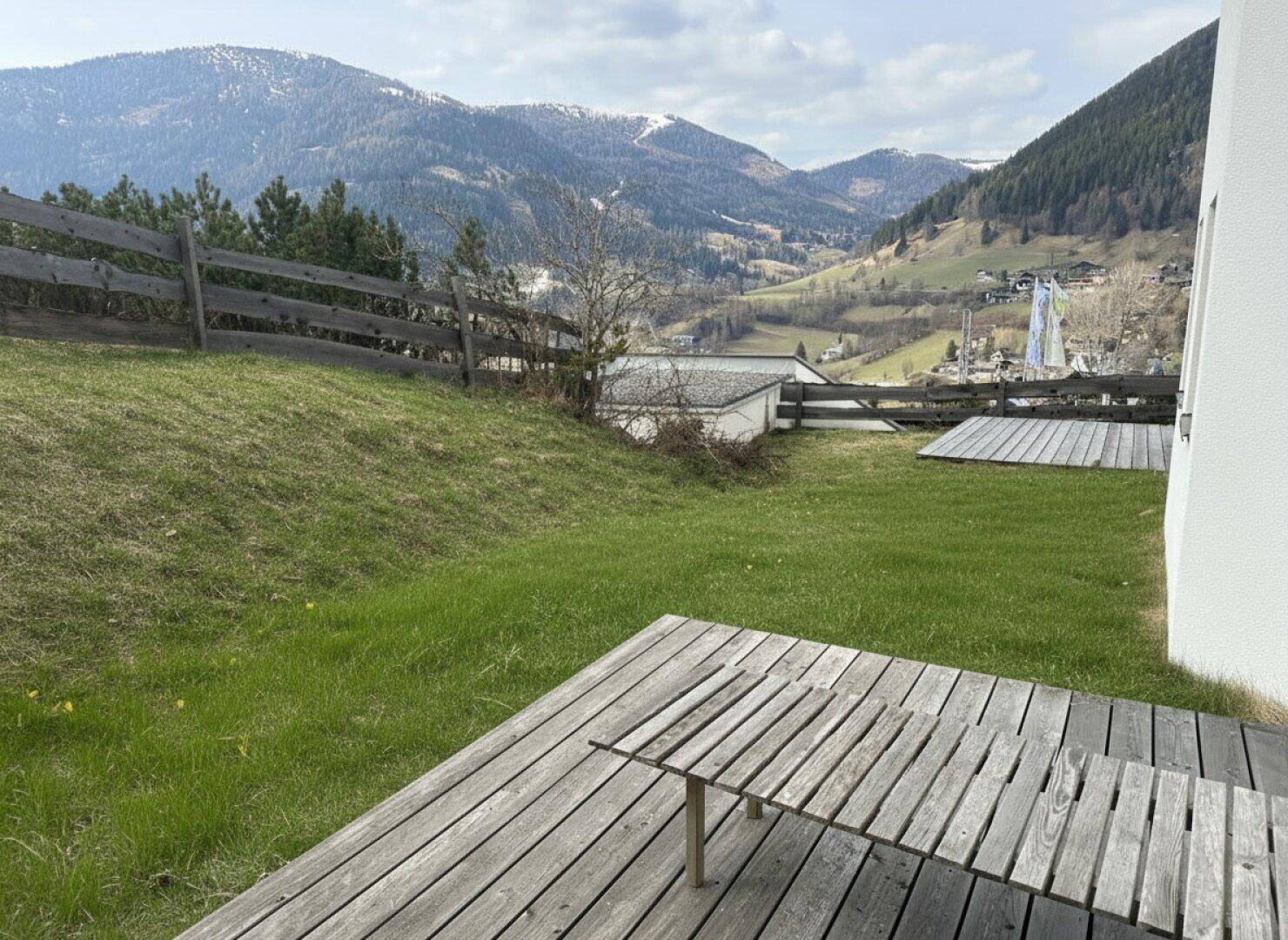 Grüne Gartenfläche mit Holzterrasse und Blick auf die malerische Berglandschaft.