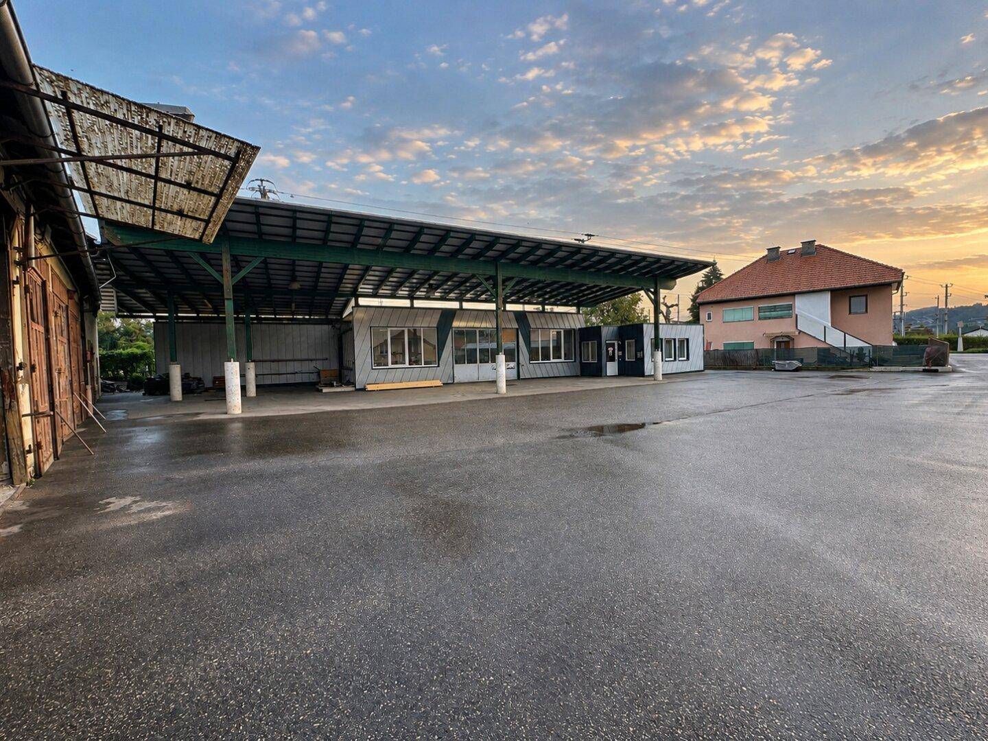 Große asphaltierte Fläche mit überdachtem Bereich und einem Gebäude im Hintergrund bei Sonnenuntergang.