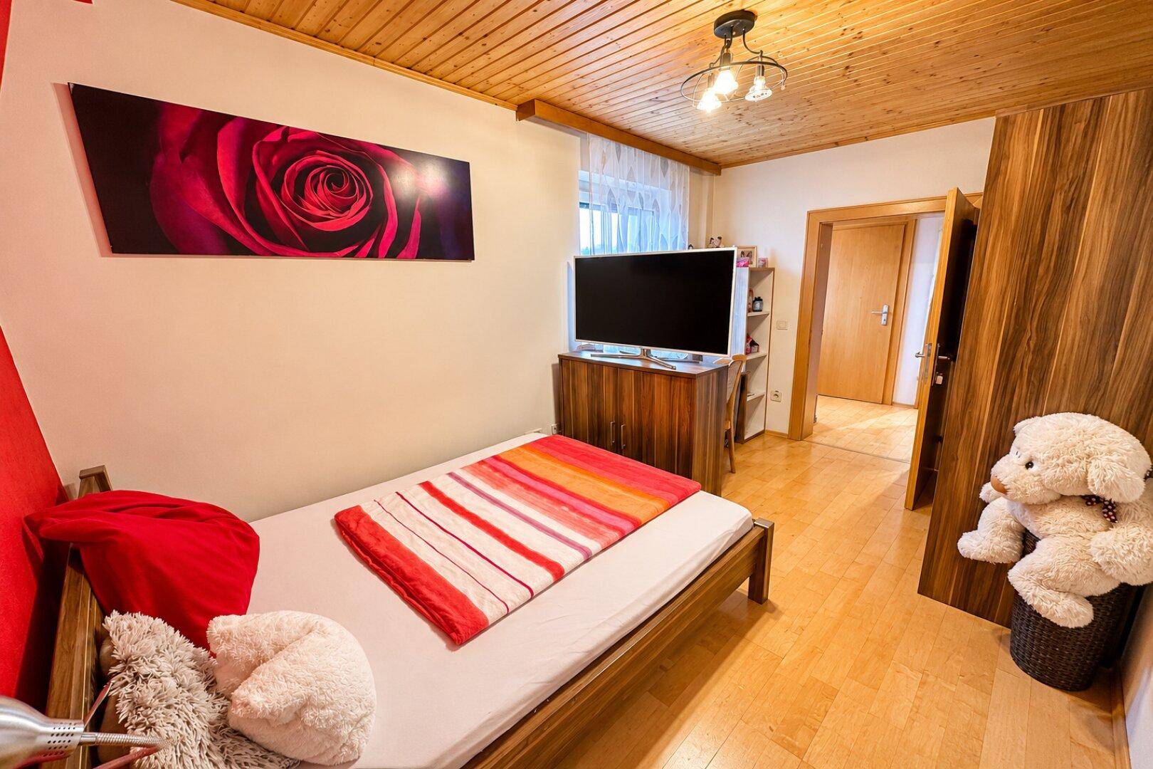Helles Schlafzimmer mit Einzelbett, Fernseher und Holzboden.