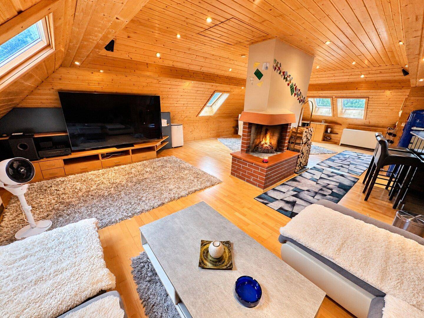 Gemütliches Wohnzimmer im Dachgeschoss mit Holztäfelung, Kamin und großem Fernseher.