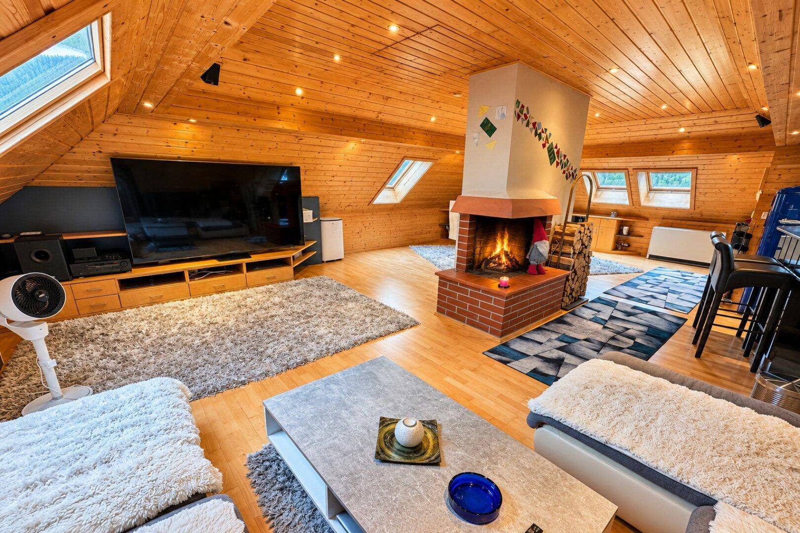 Geräumiges Wohnzimmer im Dachgeschoss mit Holzbalkendecke, Kamin und bequemen Sofas.