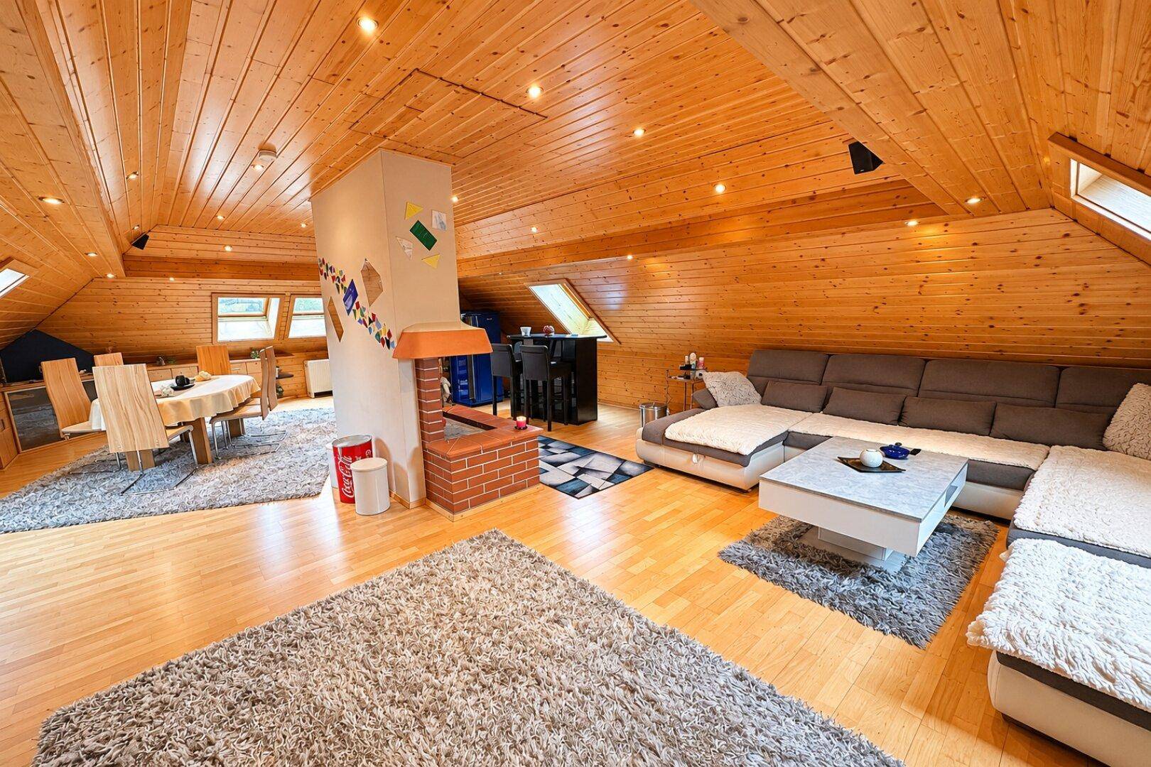 Offener Wohn- und Essbereich im Dachgeschoss mit Holztäfelung und Kamin als Raumteiler.