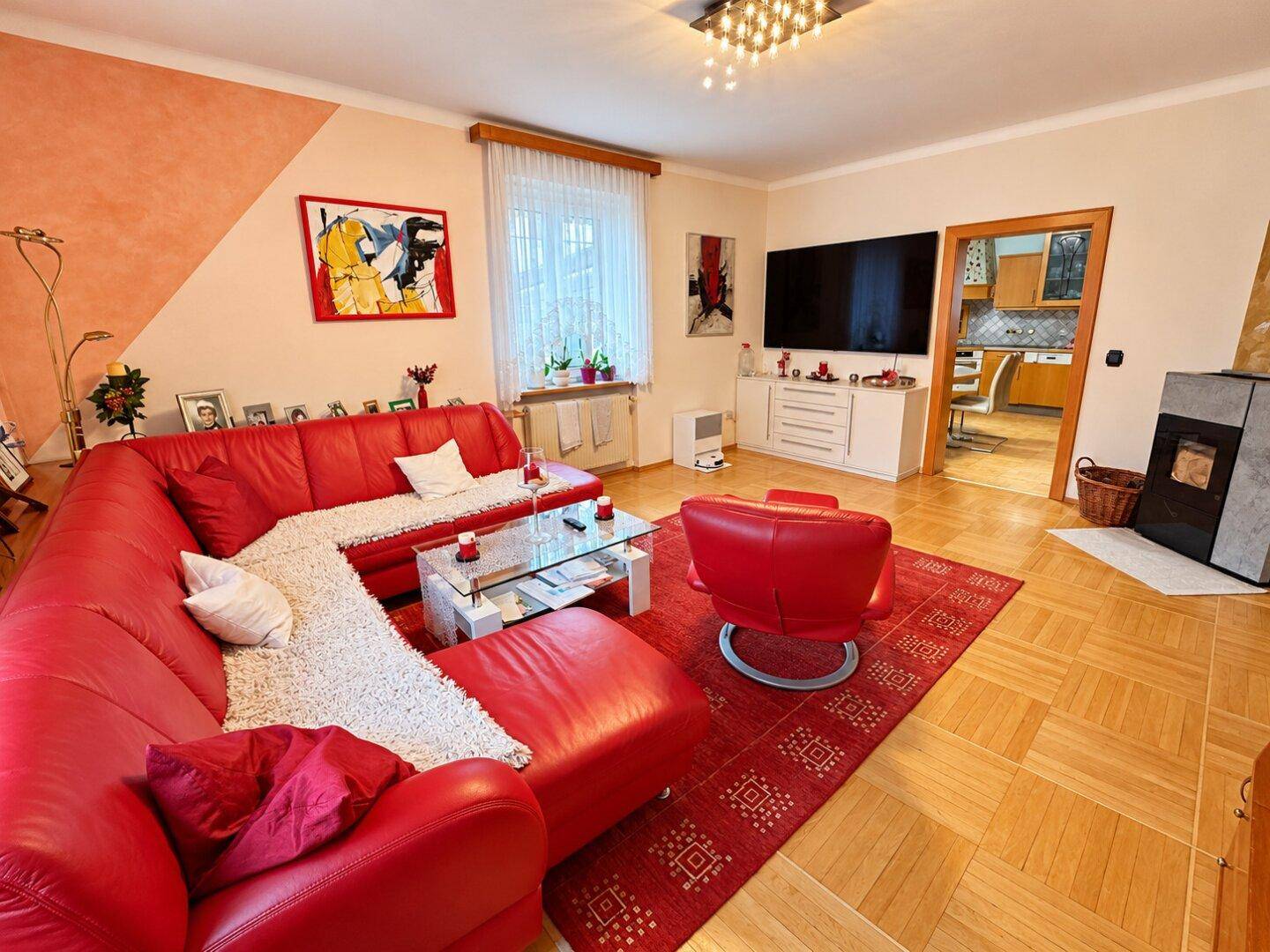 Helles Wohnzimmer mit rotem Sofa, Holzboden und kleinem Kaminofen.