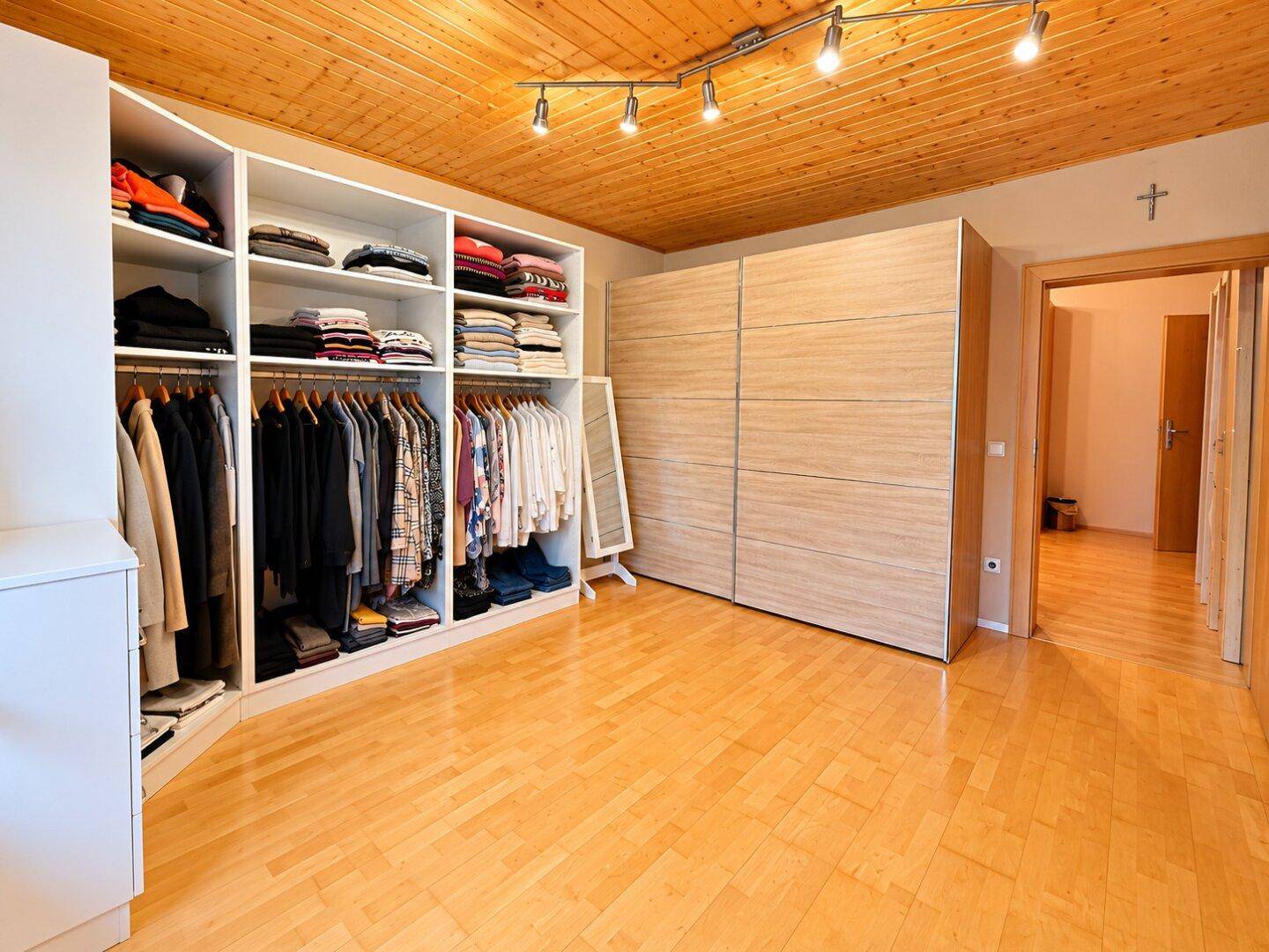 Geräumiger begehbarer Kleiderschrank mit viel Stauraum und Holzdecke.