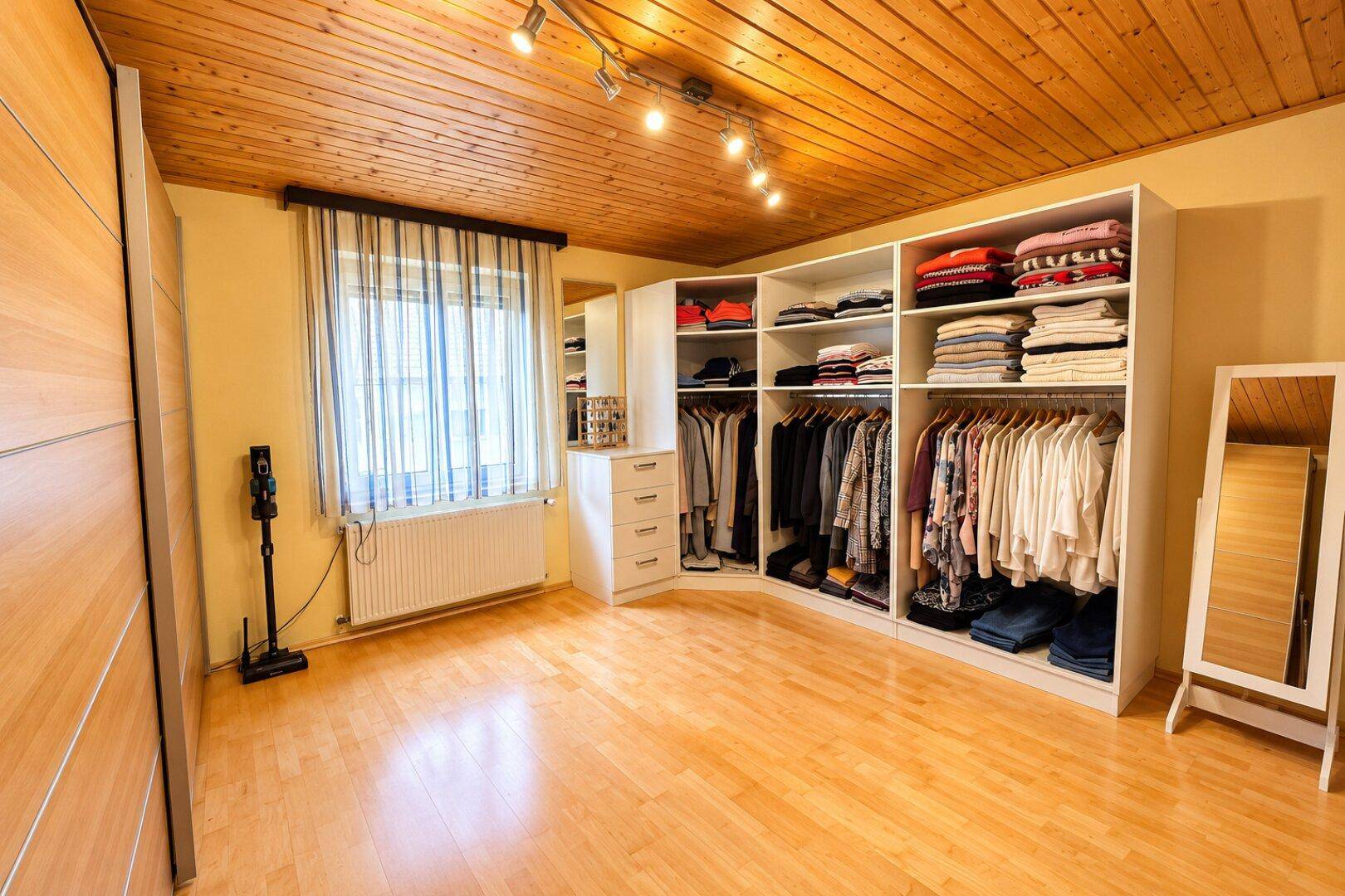 Heller begehbarer Kleiderschrank mit Fenster und viel Platz für Kleidung.
