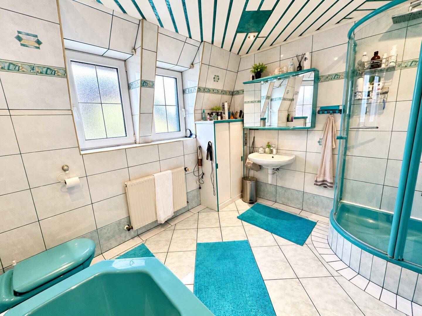 Geräumiges Badezimmer mit Badewanne, Dusche, WC und zwei Fenstern.