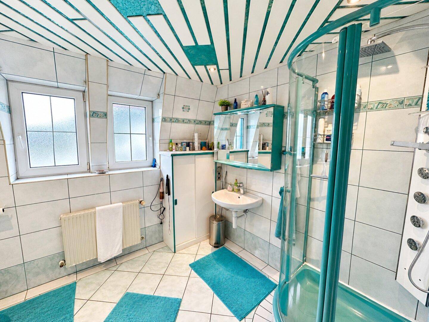Helles Badezimmer mit Dusche, Waschbecken und Fenster.