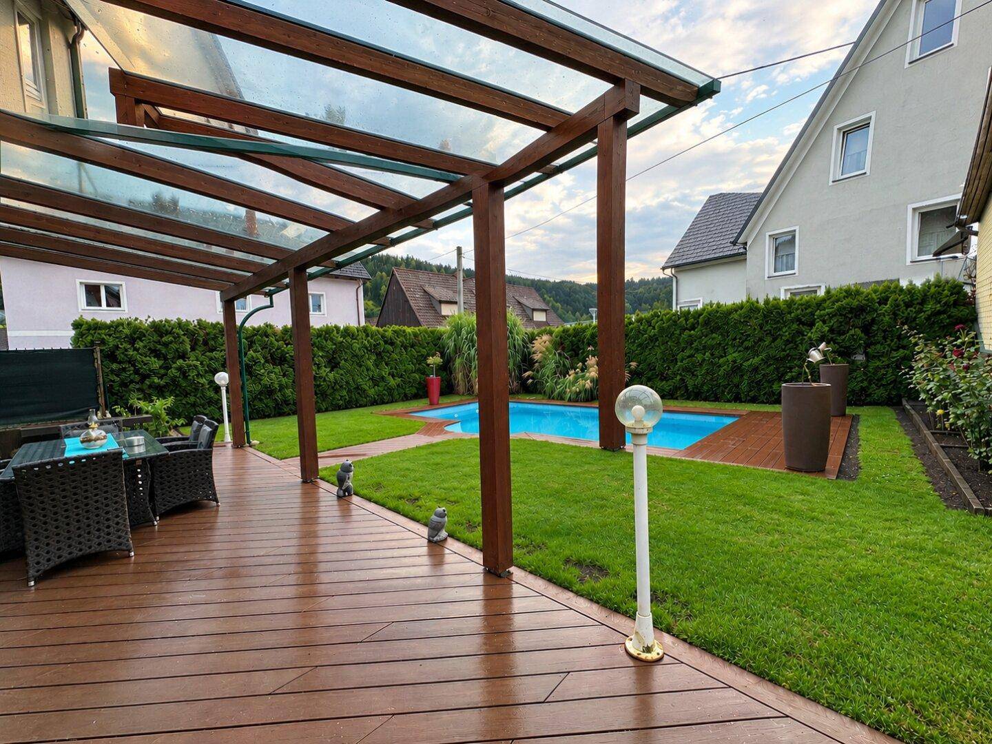 Überdachte Holzterrasse mit Sitzgelegenheiten und Blick auf den Poolbereich.