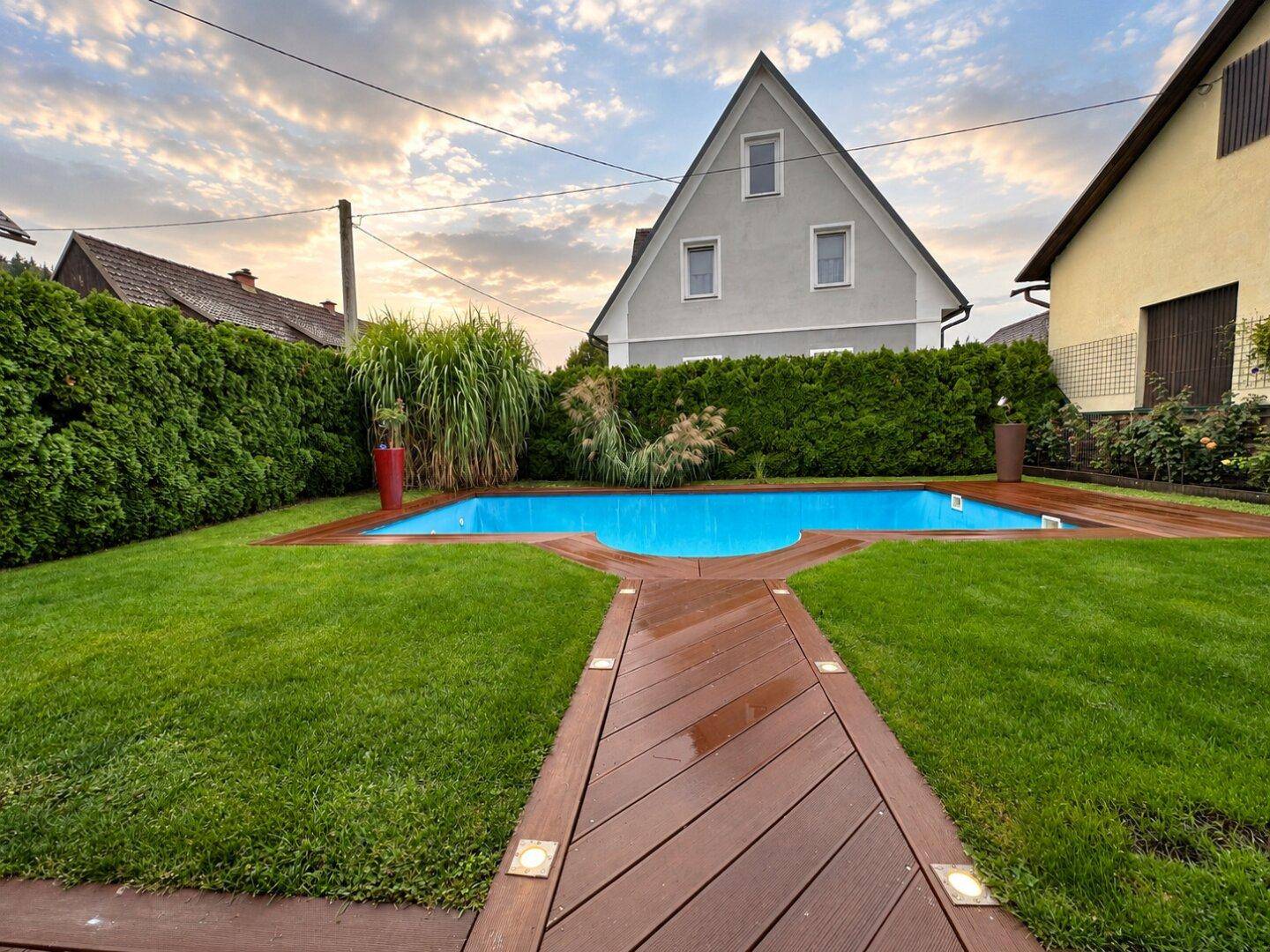 Attraktiver Garten mit Pool, Holzsteg und gepflegter Rasenfläche.