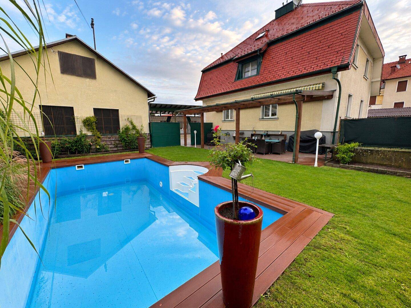 Weitläufiger Garten mit großem Swimmingpool, Rasenfläche und angrenzenden Gebäuden bei Sonnenuntergang.