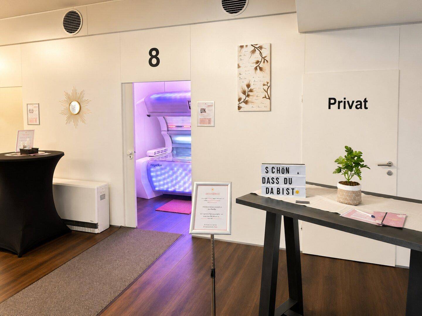 Flur mit Blick in einen Raum mit Solarium, daneben ein Tisch mit Dekoration und einem "Privat"-Schild.