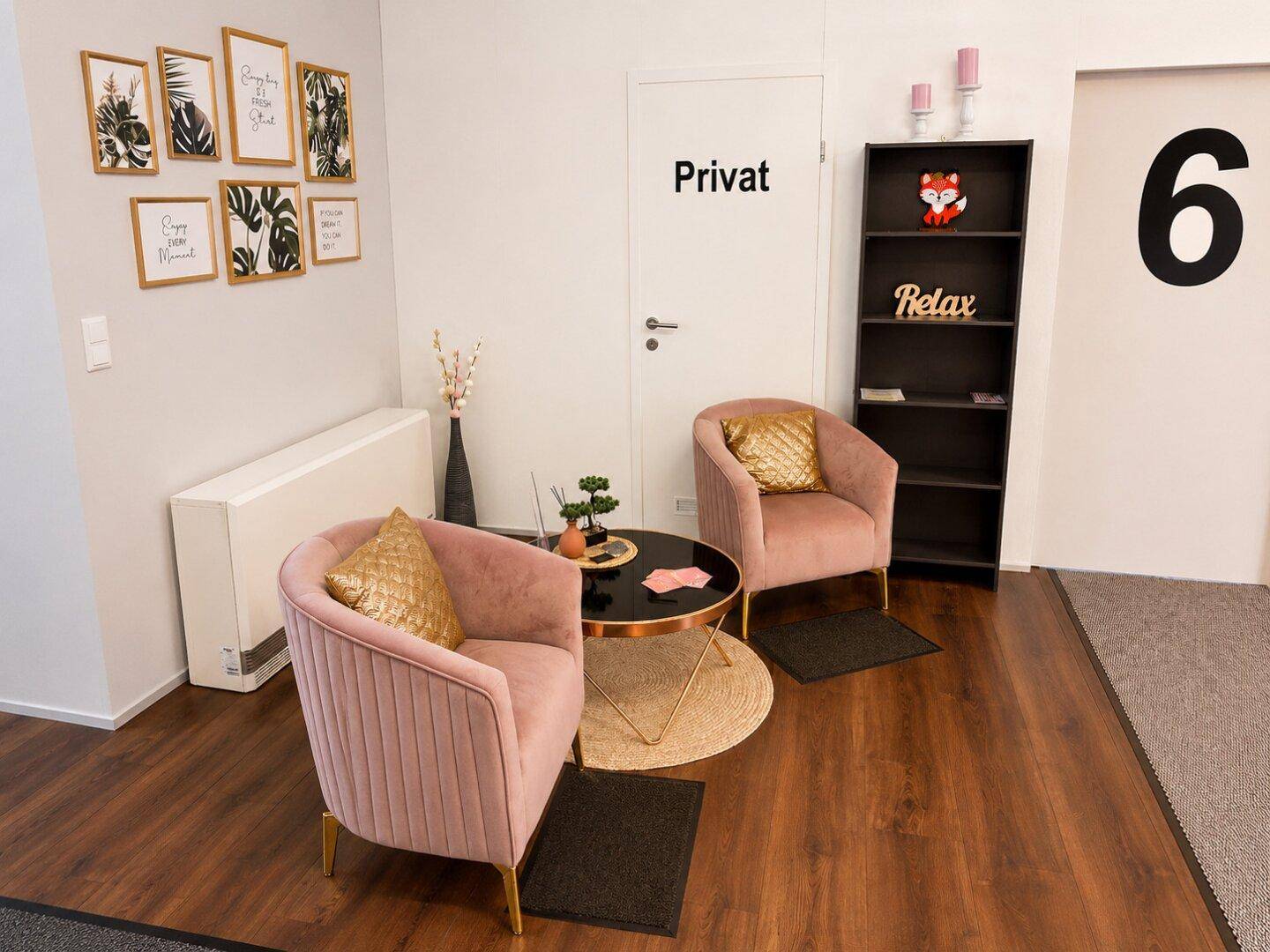 Gemütliche Sitzecke mit zwei rosa Sesseln, einem runden Tisch und Wanddekoration.