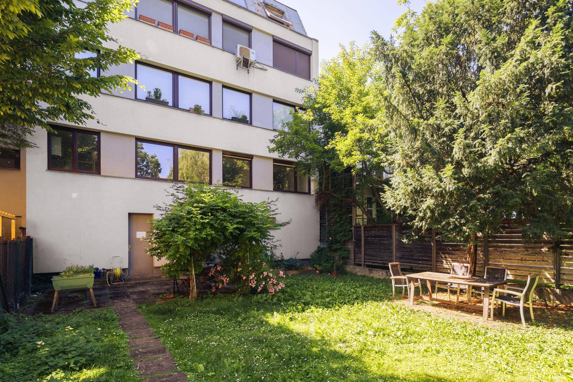 Grüner Gartenbereich mit Sitzgelegenheiten und Blick auf die Gebäudefassade.