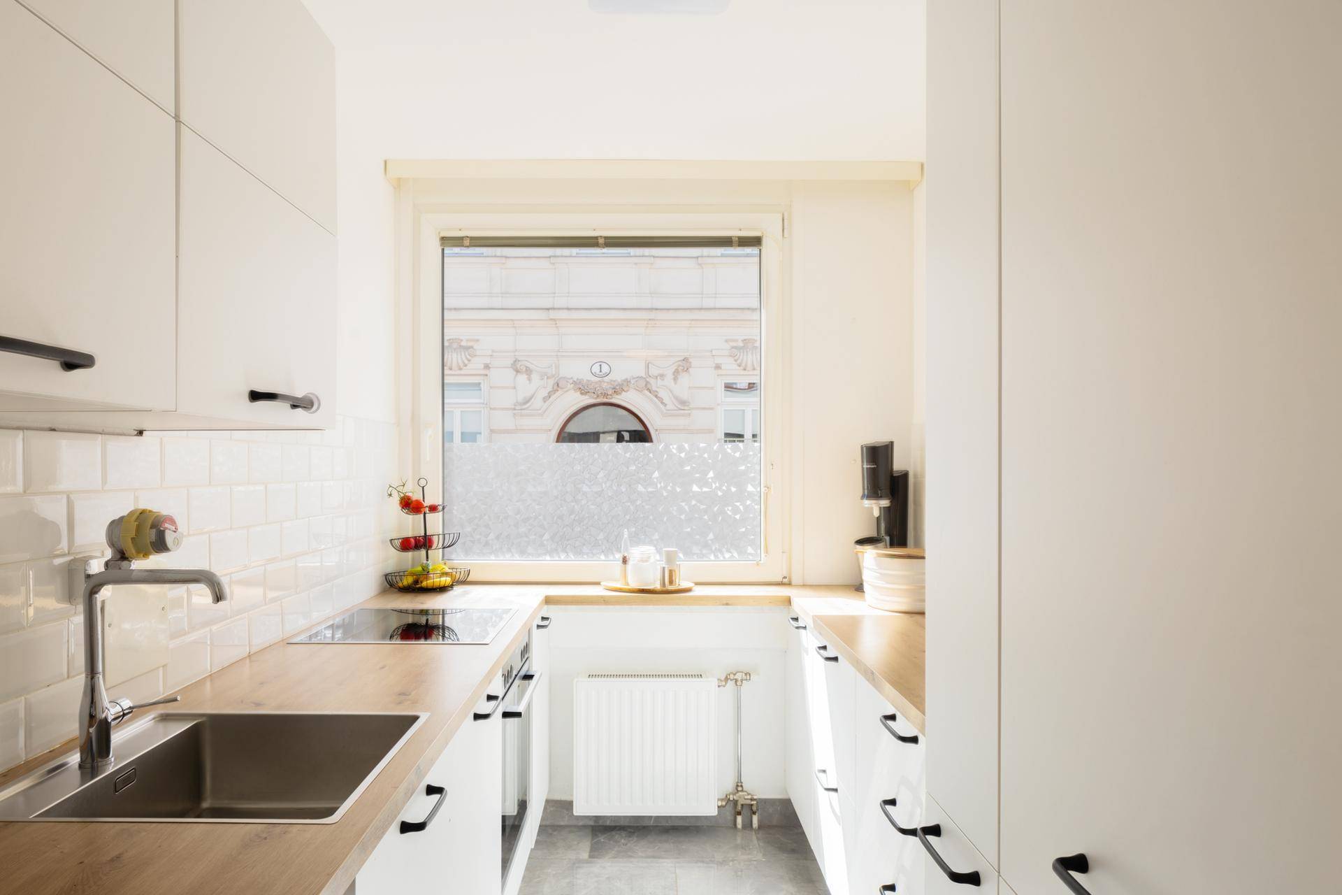 Schmale Küche mit weißen Schränken, Holz-Arbeitsplatten und Fensterblick auf die Straße.
