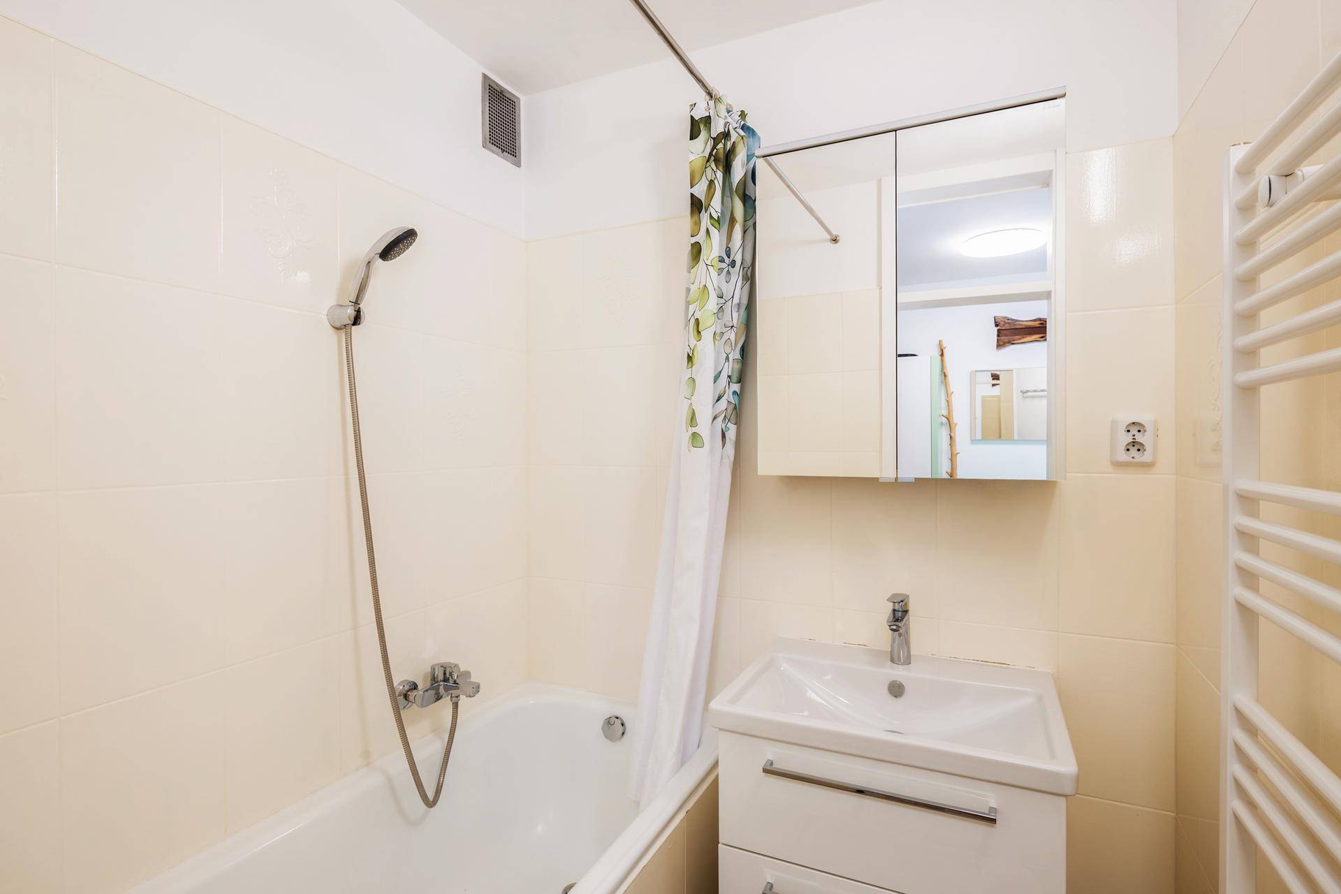 Badezimmer mit Badewanne, Duschvorhang, Waschbecken und beheiztem Handtuchhalter.