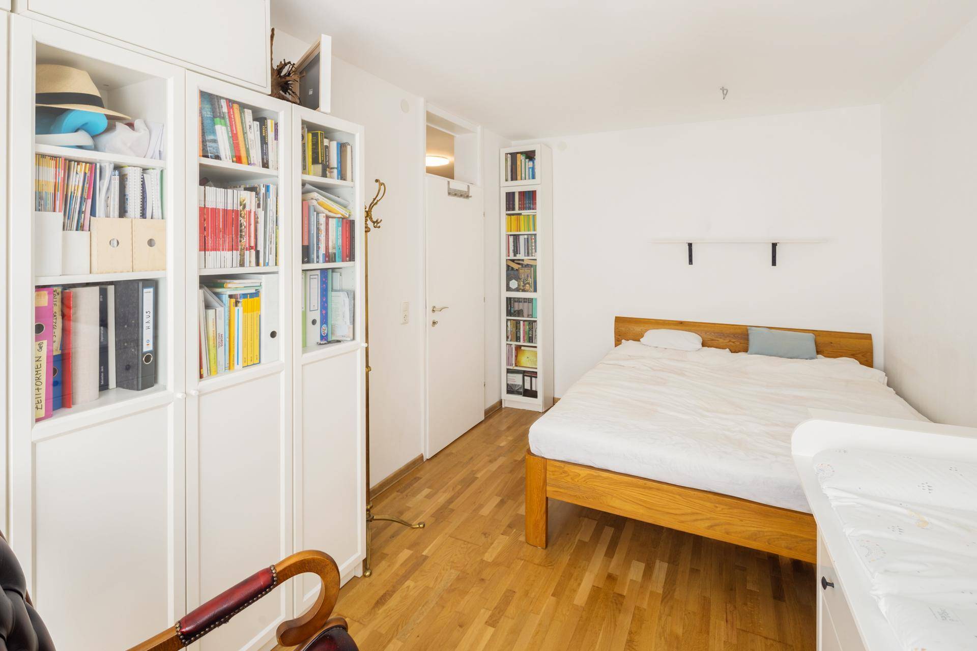 Schlafzimmer mit Holzbett, Bücherregalen und Holzboden, hell und funktional eingerichtet.