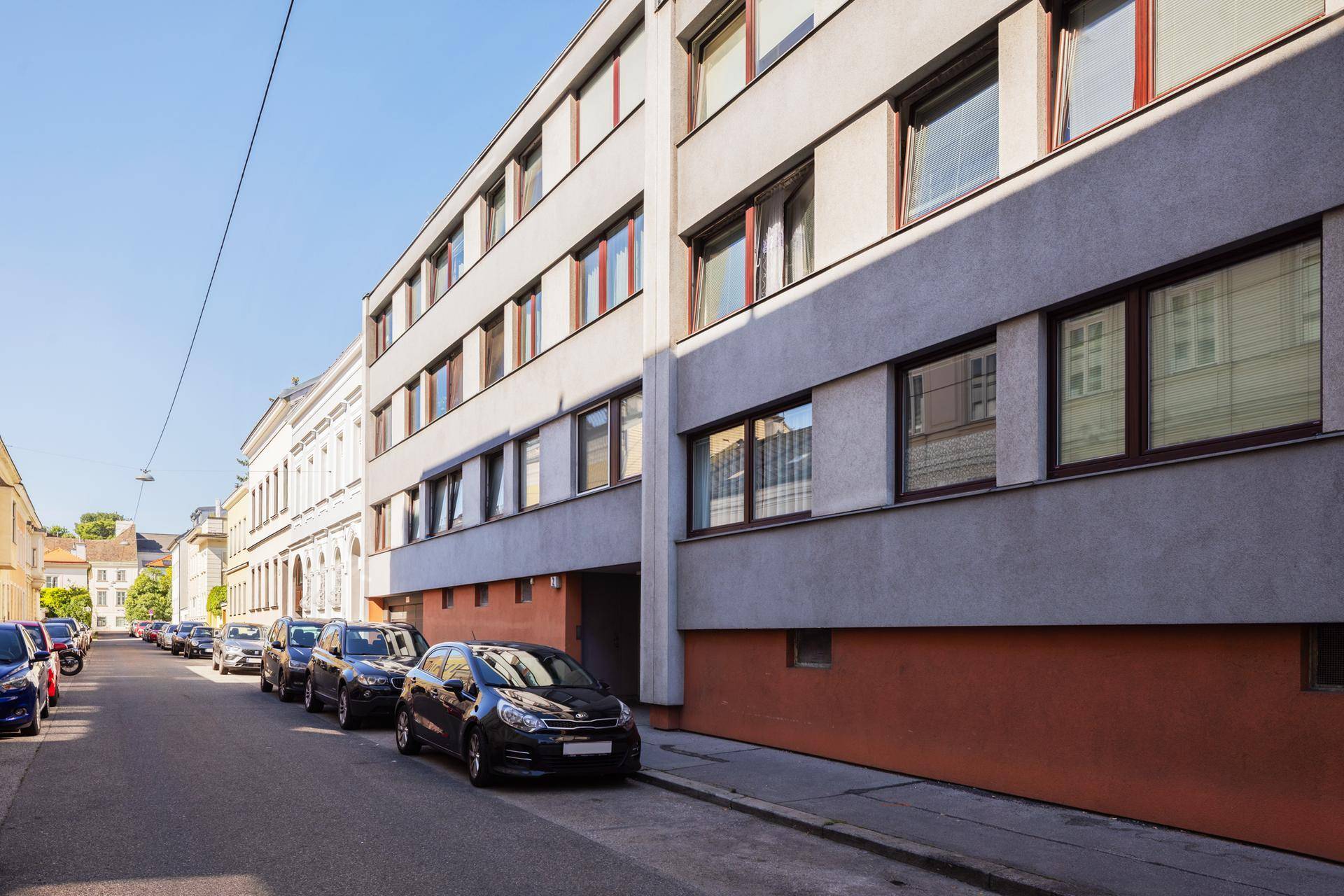 Moderne Gebäudefassade an einer ruhigen Wohnstraße mit parkenden Autos.