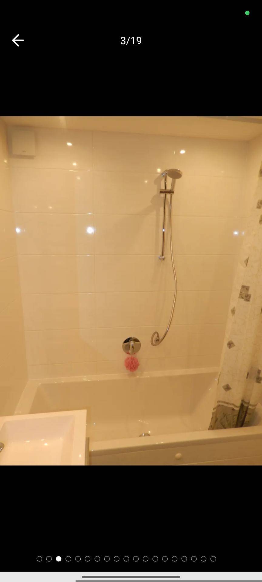 Badezimmer mit Badewanne und Duschvorrichtung, komplett in weißen Fliesen gehalten.