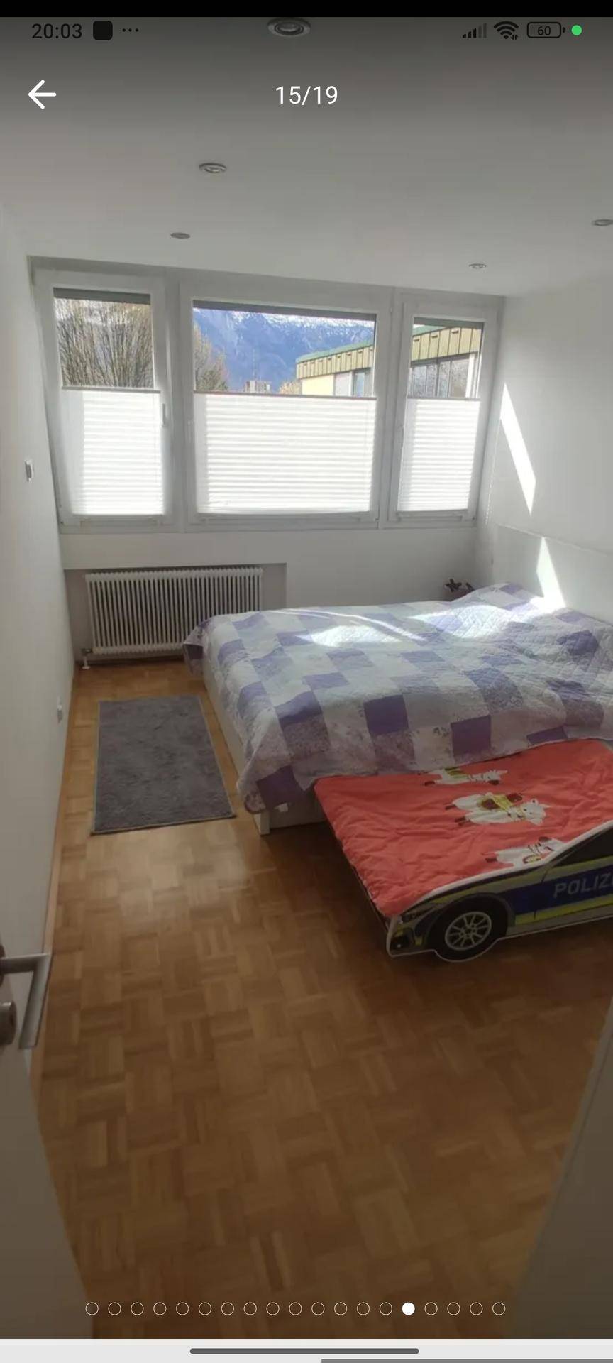 Schlafzimmer mit Bett, Heizkörper unter großen Fenstern und hellem Parkettboden.