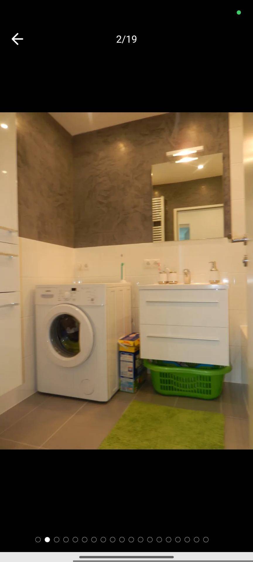 Badezimmer mit Waschmaschine, Waschbeckenunterschrank und Spiegel an gefliesten Wänden.