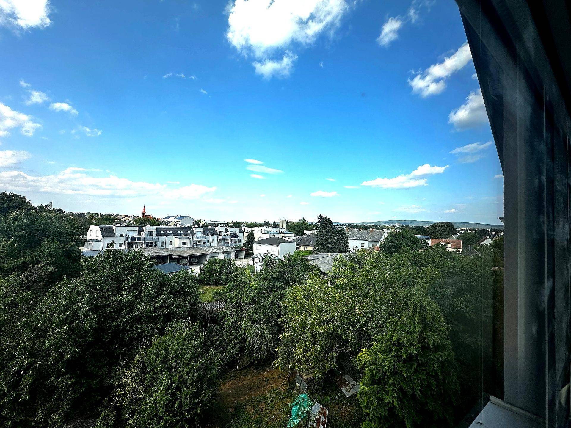 Weitblick über eine grüne Wohnsiedlung mit vielen Bäumen unter blauem Himmel.