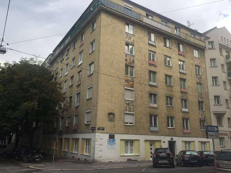 Mehrstöckiges Wohngebäude mit gelber Fassade an einer Straßenecke in städtischer Umgebung.