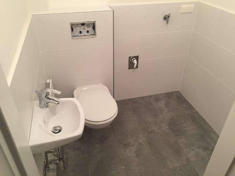 Separates WC mit wandhängender Toilette, kleinem Waschbecken und modernen grauen Bodenfliesen.