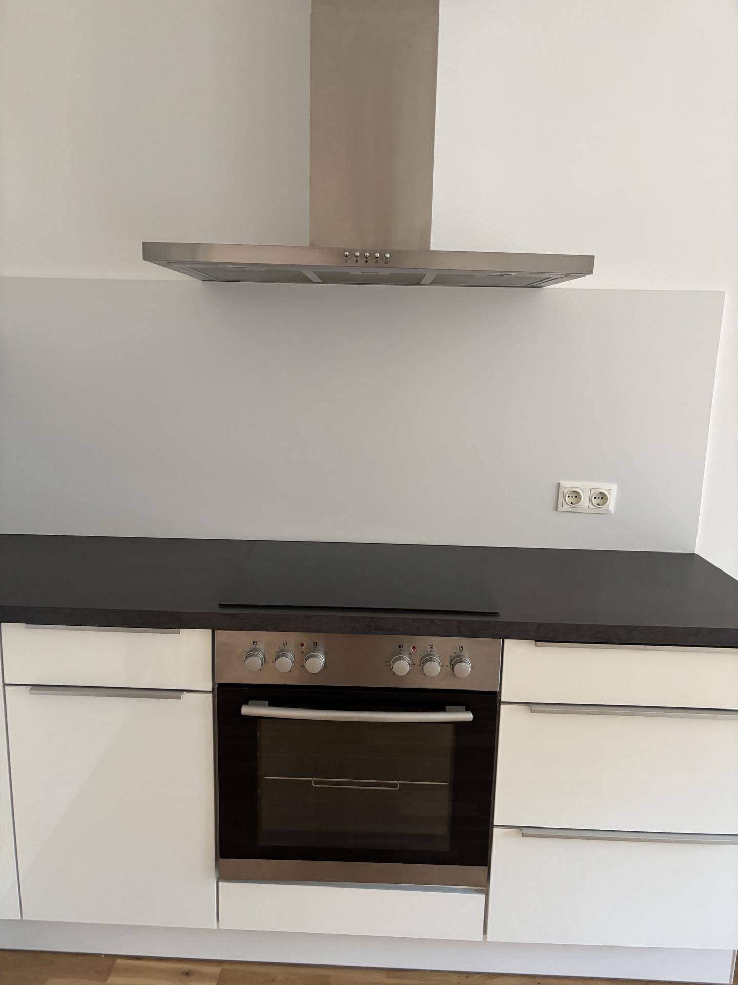 Küchenzeile mit integriertem Backofen, Kochfeld und Dunstabzugshaube, mit dunkler Arbeitsplatte.