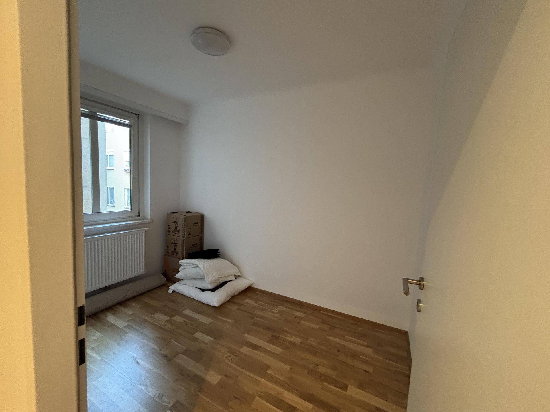 Kleines, helles Zimmer mit Holzparkettboden und Fenster, ideal als Schlaf- oder Arbeitszimmer.