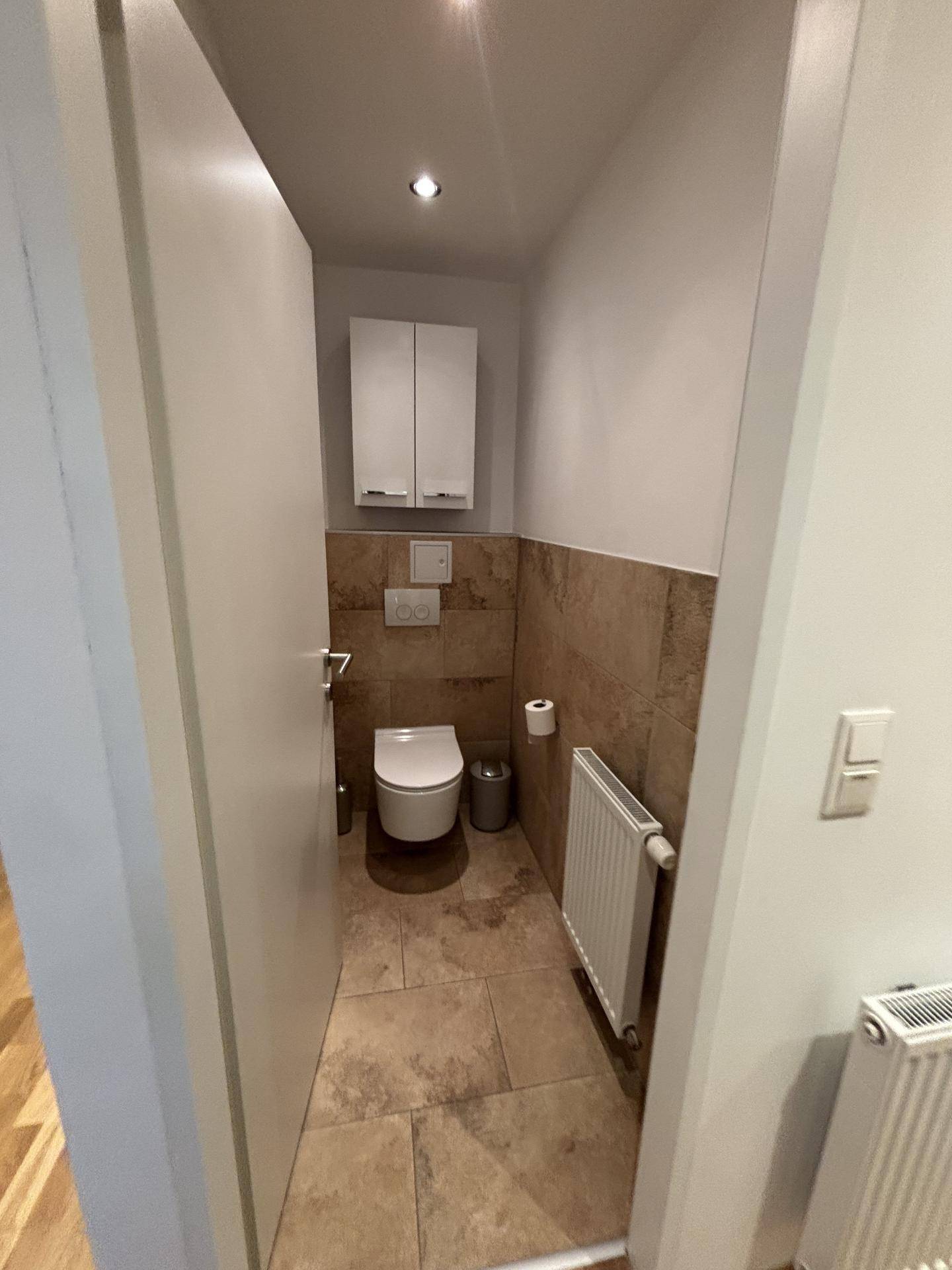 Kleines Gäste-WC mit wandhängender Toilette, Fliesenboden und einem Heizkörper.